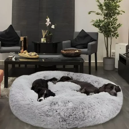 Twee honden rusten samen in een groot, lichtgrijs anti-stress donut bed in een gezellige woonkamer.