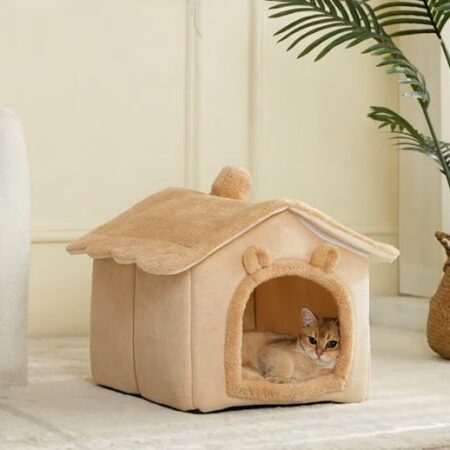 Kat ligt ontspannen in beige kattenhuisje met oortjes en golvend dak, in een rustige woonkamer.